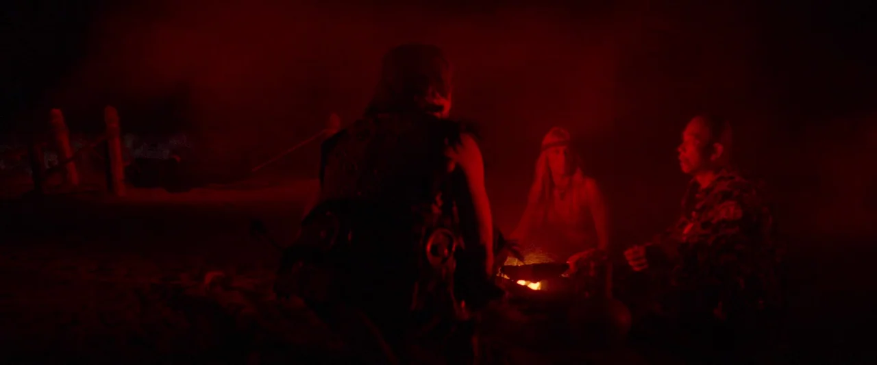 Conan The Barbarian (1982) movie still: medium — A group of three people sits around a small fire in a dark outdoor setting. They remain gathered…