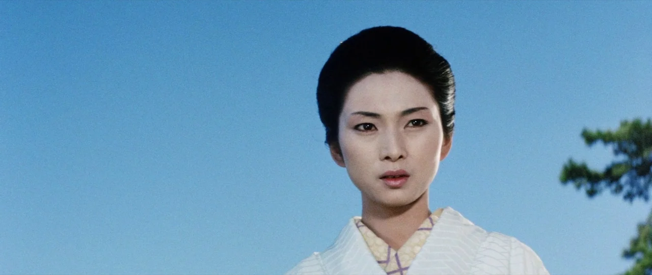 Lady Snowblood (1973) movie still: closeup — A woman stands against a bright, cloudless blue sky with hints of tree foliage. She wears a traditional…