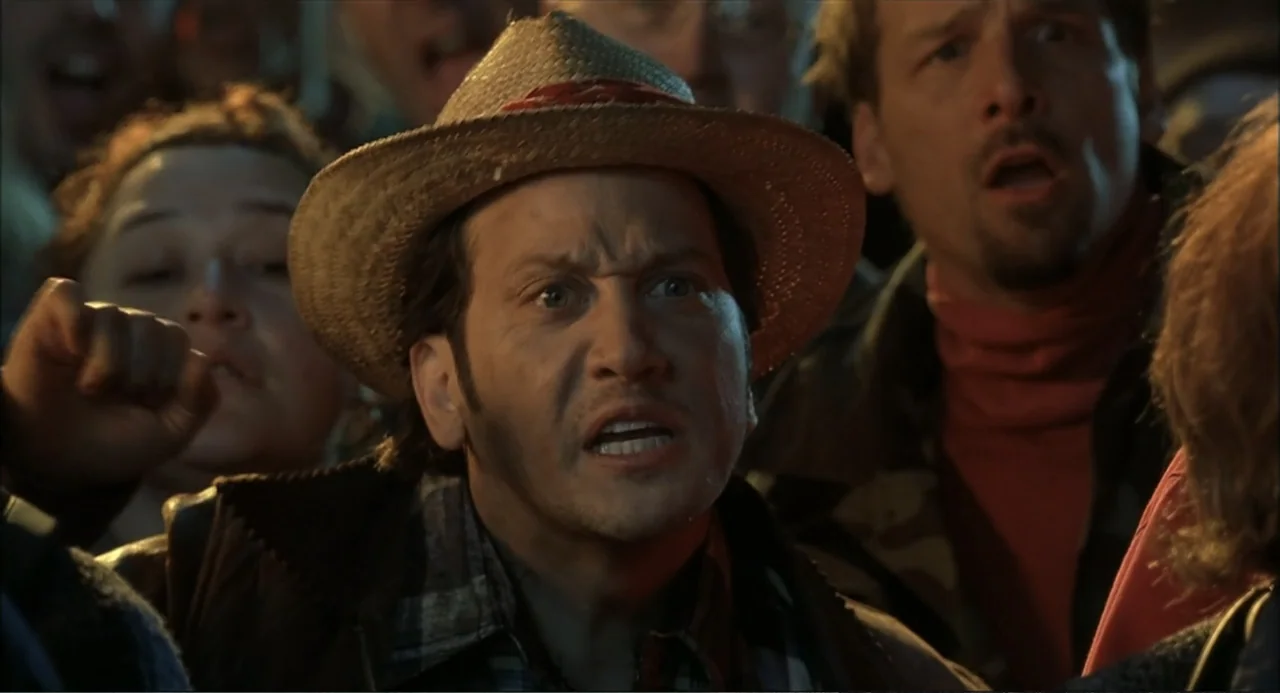 Little Nicky (2000) movie still: closeup — A man stands in a dense crowd of people in a dimly lit space. He yells with a distressed expression while…