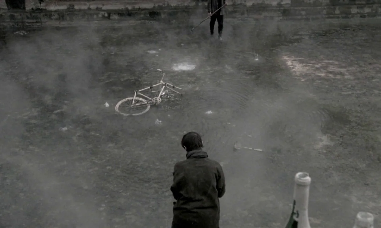 Nostalghia (1983) movie still: wide — A murky, shallow body of water covered in mist contains a submerged white bicycle. A man stands in the…
