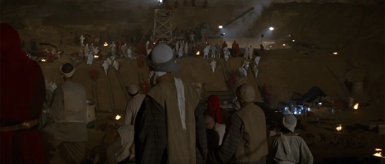 The Mummy Returns (2001) movie still: wide — A deep archaeological pit at night is crowded with laborers in traditional middle-eastern attire. The…