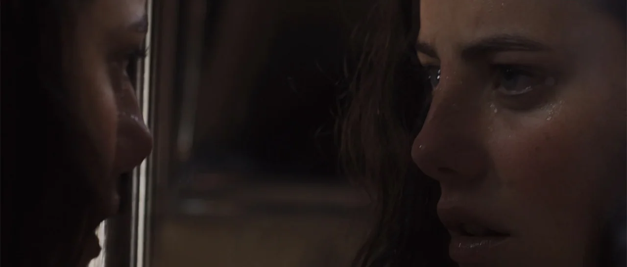 The Truth About Emanuel (2013) movie still: closeup — A dark indoor space features a glass pane acting as a reflective surface. A young woman with…