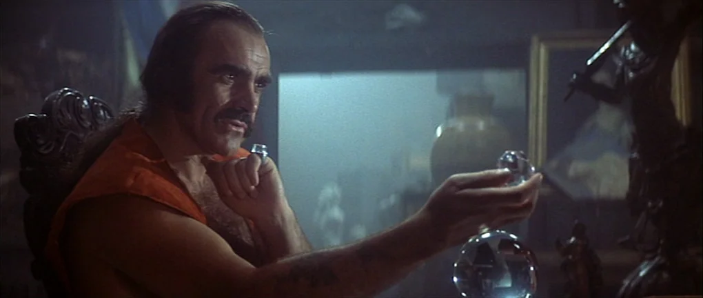 Zardoz (1974) movie still: medium — A dimly lit room filled with shadowy antique artifacts and indistinct display objects. A man with a dark…