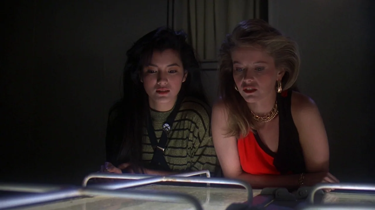 Friday the 13th Part VIII: Jason Takes Manhattan (1989) movie still: medium — Two women lean over a glowing tabletop surface in a dark room. They…