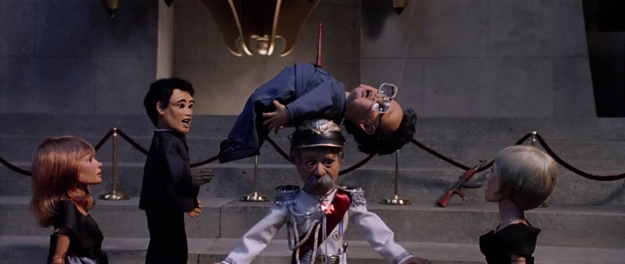 Team America: World Police movie still: wide — A stone memorial interior features a red velvet rope and a rifle leaning against steps. Four puppet…