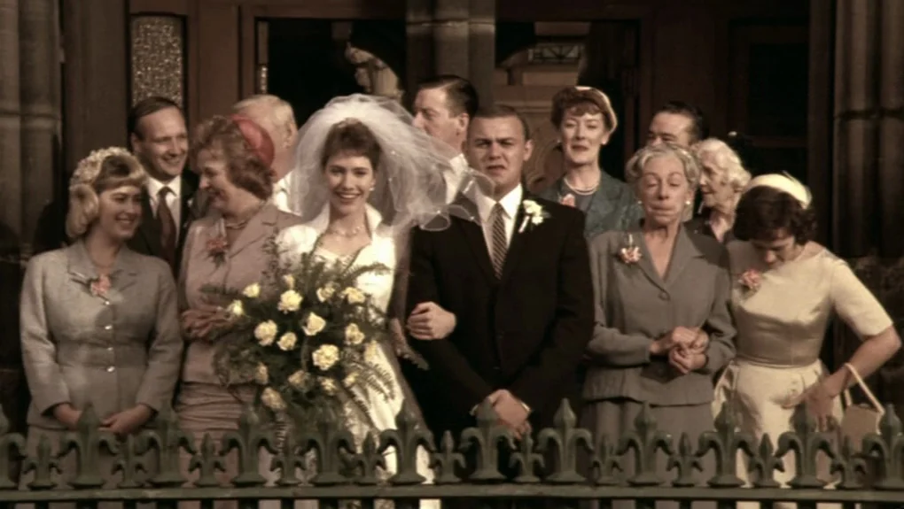 Distant Voices, Still Lives (1988) movie still: medium — A group of people dressed in mid-century formal attire stand outside a stone entrance. The…
