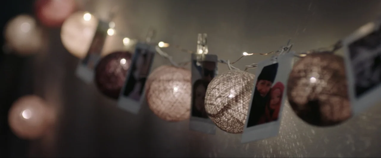 The Lie (2018) movie still: closeup — A string of decorative cotton ball lights hangs horizontally against a dark wall. Several small square…