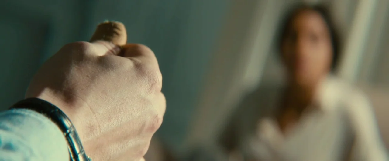 Trance (2013) movie still: closeup — A close-up shot focuses on a hand holding a small, textured object. A blurred person stands in the background,…