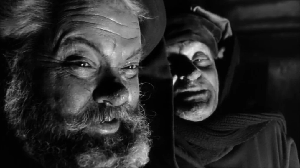 Falstaff (Chimes at Midnight) (1965) movie still: closeup — An dimly lit space featuring two men with intense expressions captured in close-up. They…