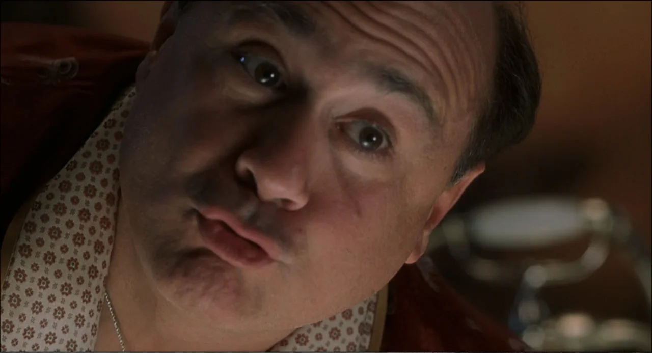 What's the Worst That Could Happen? (2001) movie still: closeup — A man looks down at the camera within a private interior space. The man has pursed…