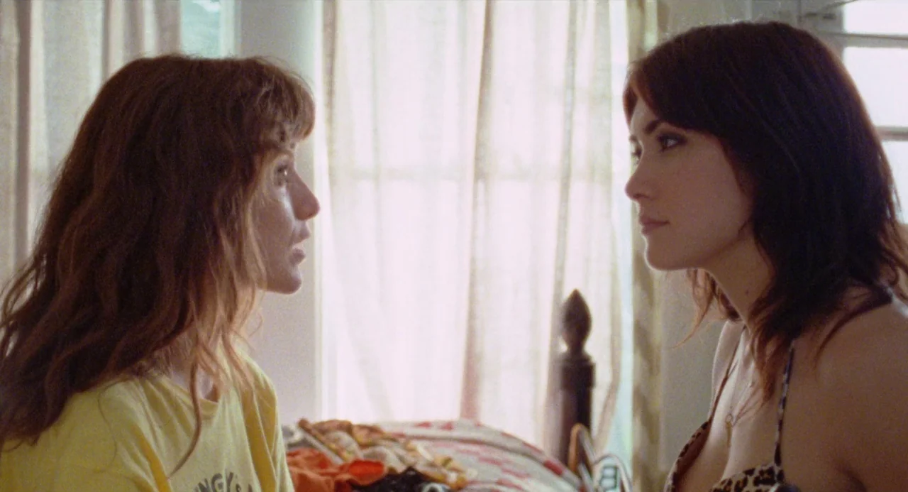 Mr. Roosevelt (2017) movie still: medium — A light-filled room features sheer curtains covering a window backdrop. Two women face each other in a…