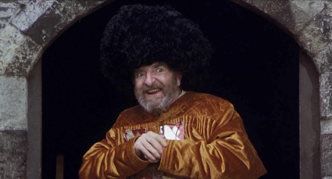 The Canterbury Tales (1972) movie still: medium — A man stands within the dark opening of a weathered stone archway. He smiles widely while wearing…