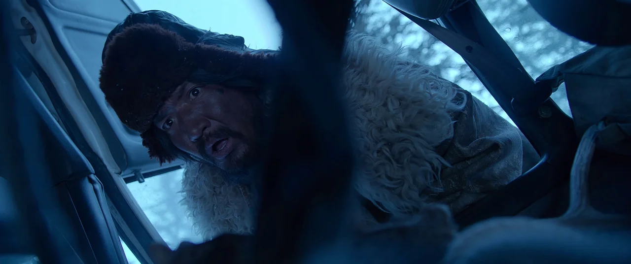 One And Four (2021) movie still: medium — A man looks inside the cabin of a vehicle through an open window. He wears a heavy winter hat and a…