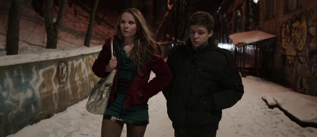 The Tribe (2014) movie still: fullbody — A narrow alleyway covered in snow features graffiti-covered concrete walls on both sides. A young couple…