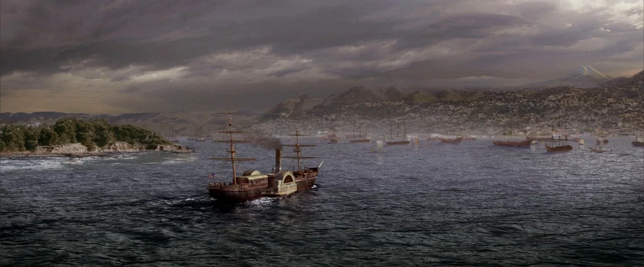 The Last Samurai (2003) movie still: wide — A steam-powered paddle wheel ship navigates calm dark waters toward a hilly coastal settlement. Multiple…