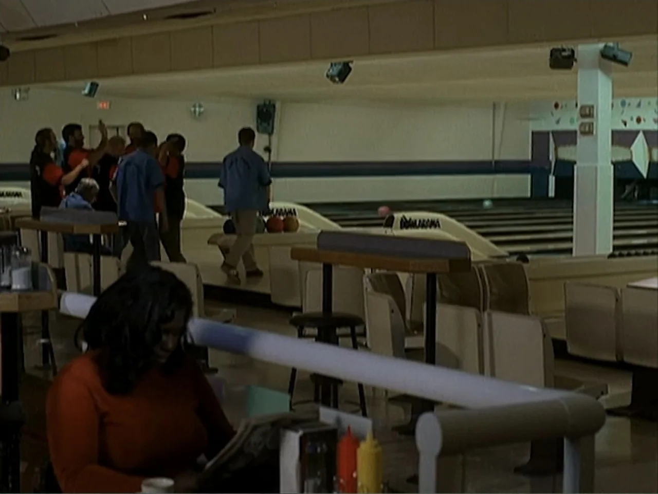 Catch a Falling Star (2000) movie still: medium — A quiet indoor bowling alley features rows of seating and wooden floor lanes. A woman sits at a…