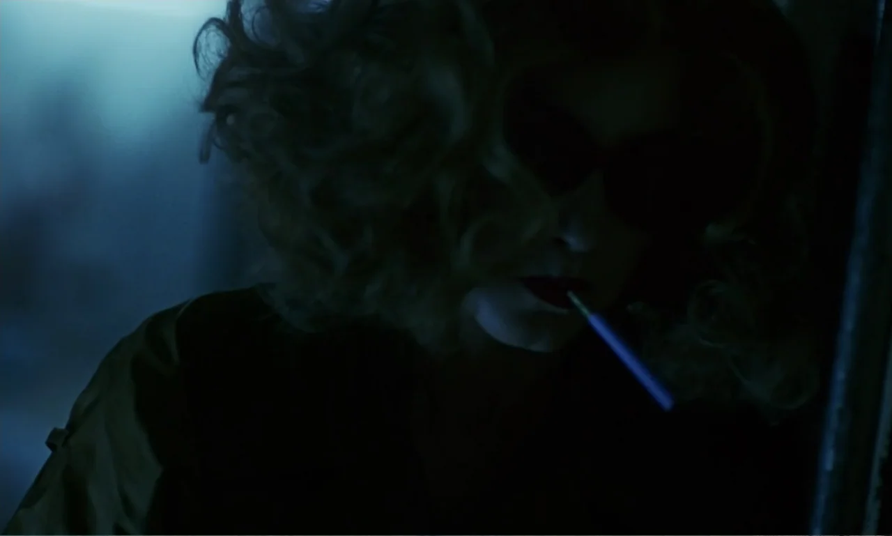 Chungking Express (1994) movie still: closeup — A dimly lit interior space with cool shadows cast over the subject. A woman with blonde curly hair…