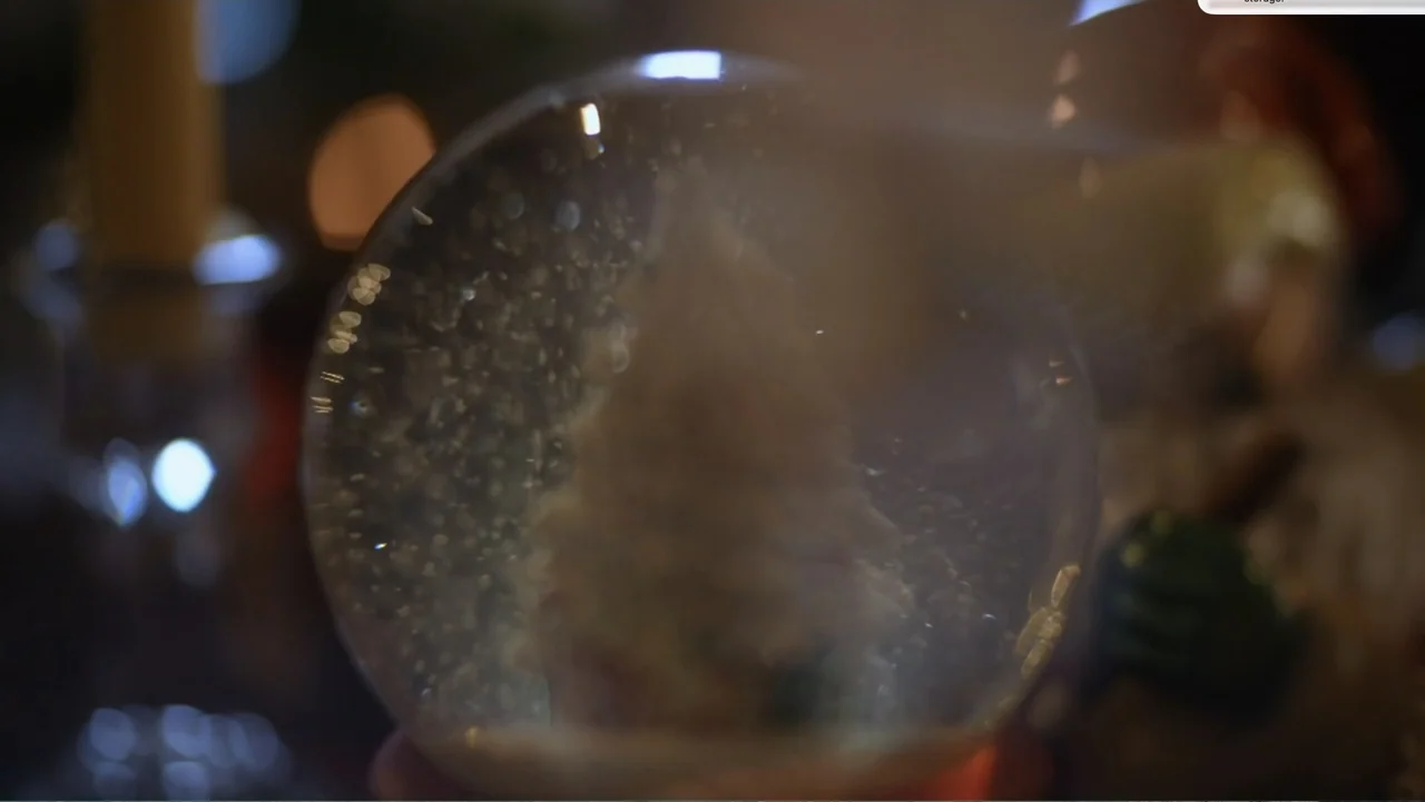 Murder at Carter County Mines (2023) movie still: closeup — A glass snow globe containing a small model tree sits in a dark room. The globe is…