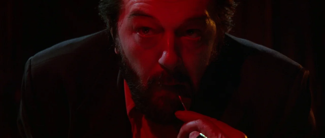 The Cook, The Thief, His Wife & Her Lover (1989) movie still: closeup — A man stands in a dark space filled with deep red light. He looks directly…