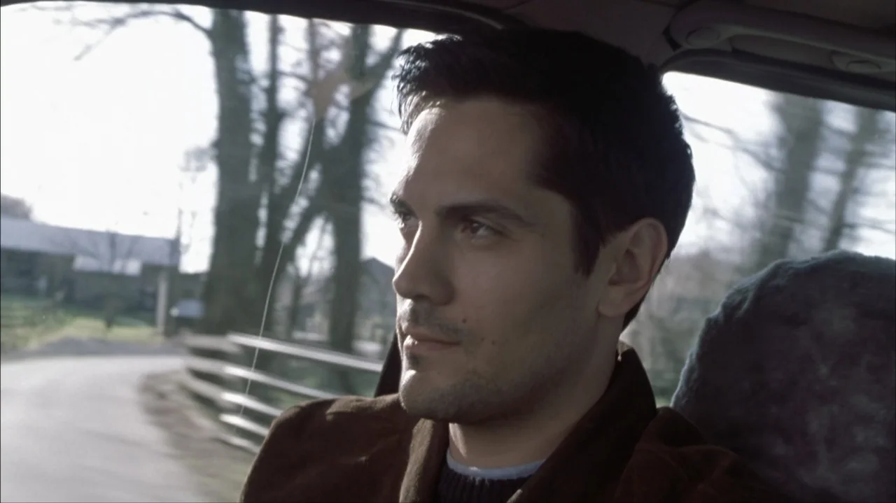 Final Destination 2 (2003) movie still: medium — A man sits inside a moving car with trees passing by outside the window. The subject focuses his…