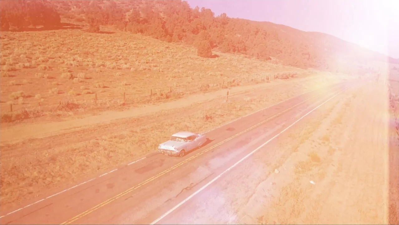 Alien Abduction: Betty and Barney Hill (2022) movie still: wide — An aerial view of a vintage car driving on a lonely asphalt highway. Dry grass…