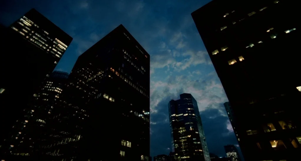 The Adjustment Bureau (2013) movie still: establishing — Tall skyscrapers dominate the night sky with illuminated windows dotting the dark…