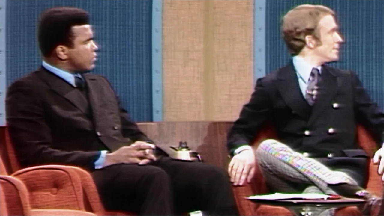 Ali & Cavett: The Tale of the Tapes (2018) movie still: medium — A 1970s television talk show set features two men sitting in orange chairs. The men…