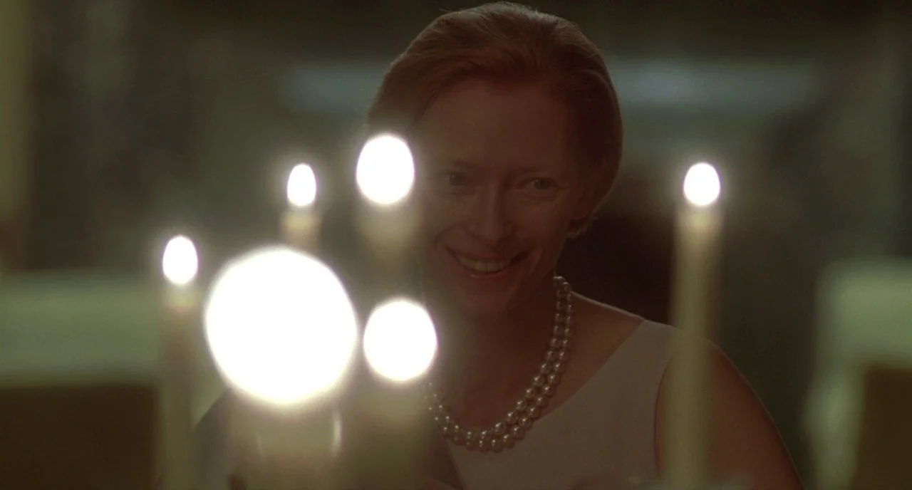 Making of: I Am Love (2009) movie still: closeup — A dimly lit dining room features a table set with several lit candles. A woman wearing pearls…