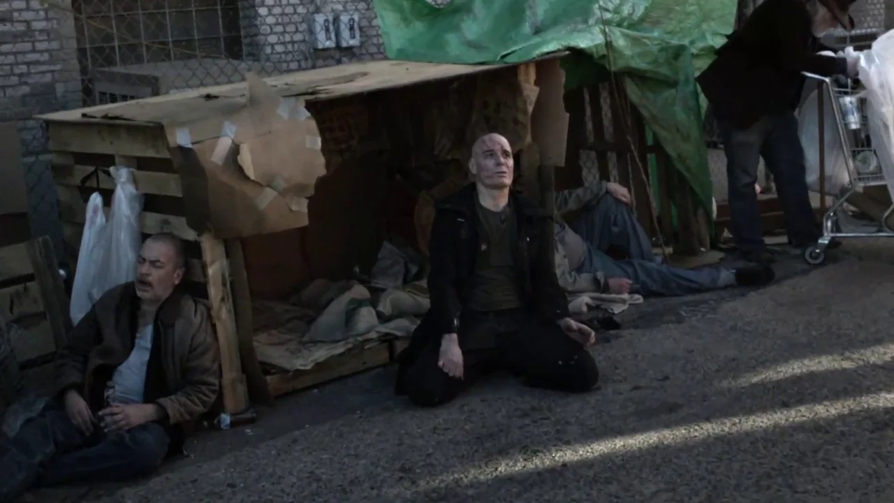 Hellraiser: Judgement (2018) movie still: fullbody — A makeshift shelter built from cardboard boxes and wood pallets sits on a sidewalk. Three…