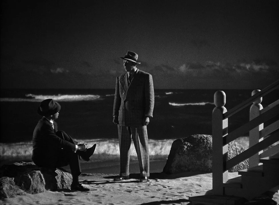 Murder, My Sweet (1944) movie still: fullbody — A sandy beach at night bordered by a staircase and dark ocean waves. Two men in fedoras and suits…