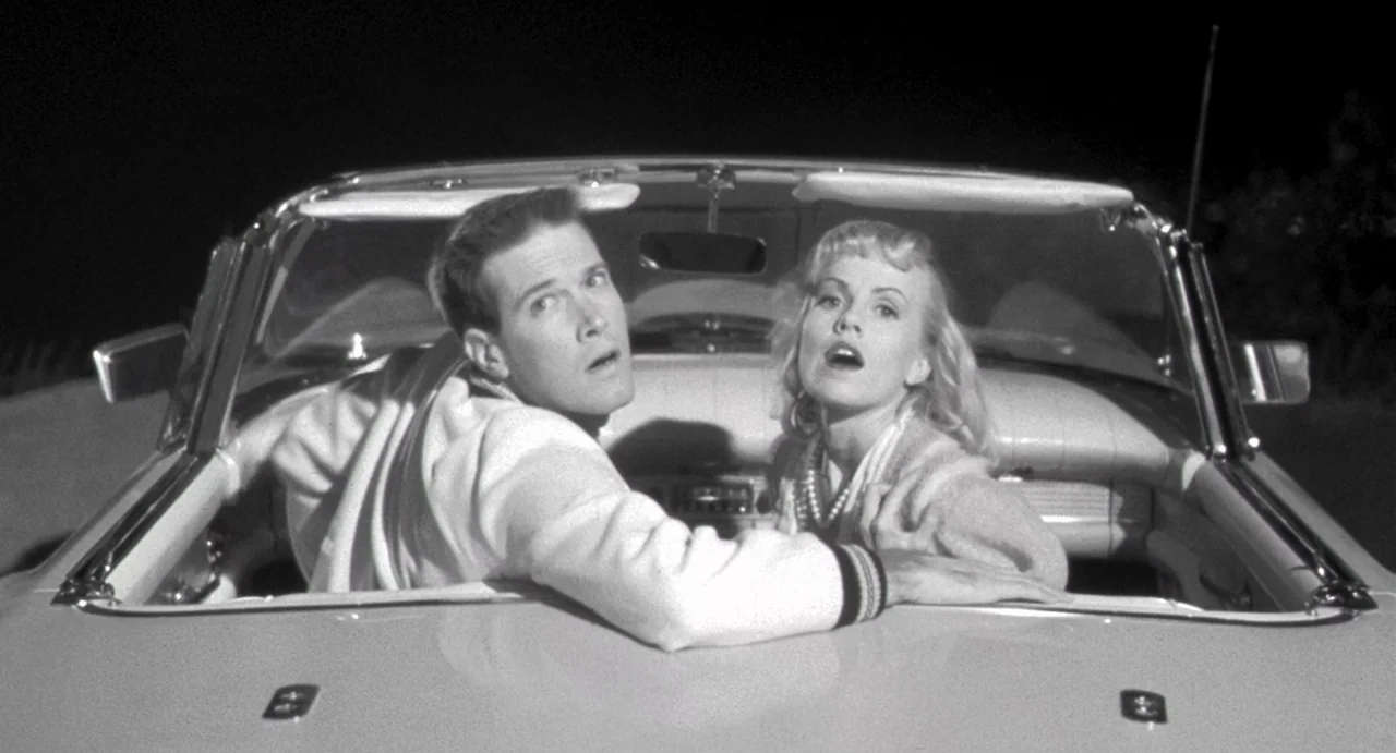 Night of the Creeps (1986) movie still: medium — A man and woman sit inside a vintage convertible car at night. They look toward the camera with…