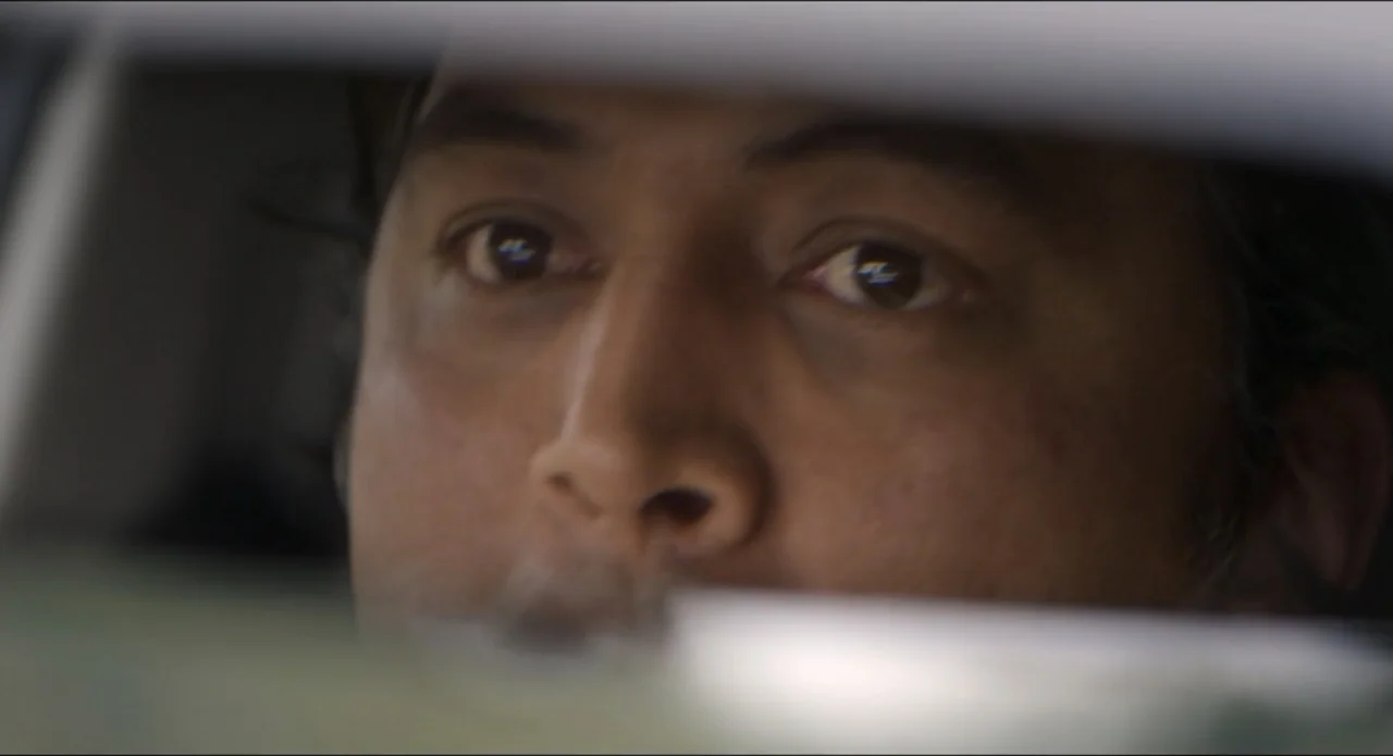 The Beauty and the Moody (2022) movie still: closeup — The interior of a vehicle with a view focused on the driver's face. The subject looks ahead…