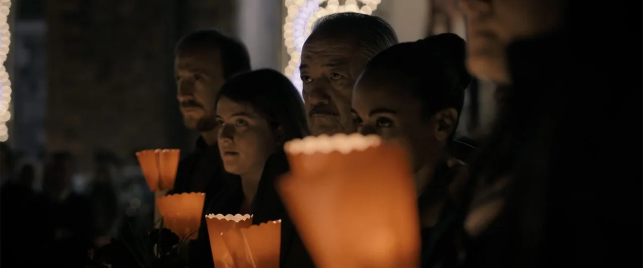 The Equalizer 3 (2023) movie still: medium — A group of people stand together in a dimly lit indoor space at night. They hold bright orange candles…