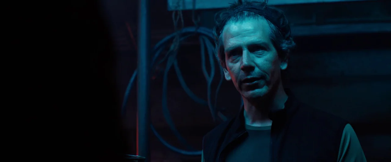 Black Sea (2014) movie still: medium — A dark, industrial garage space illuminated by sharp, colorful artificial light sources. A middle-aged man…