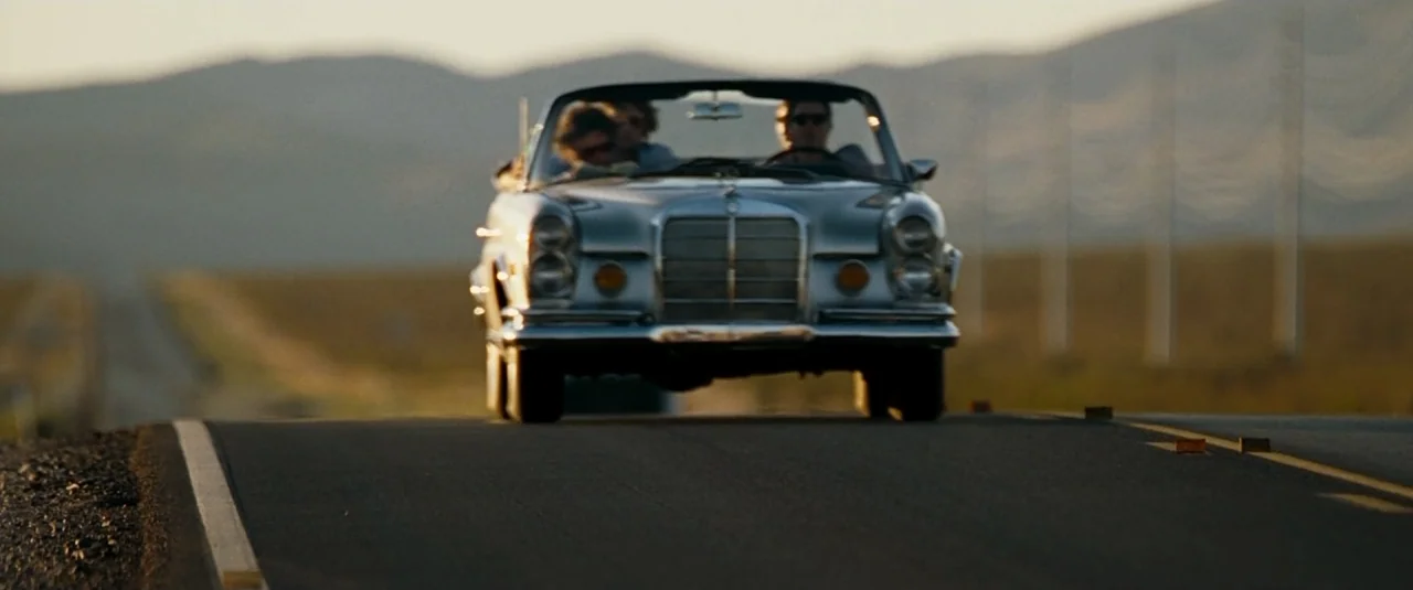 The Hangover (2009) movie still: wide — A vintage convertible travels down a desert highway during golden hour. Mountains are visible in the…