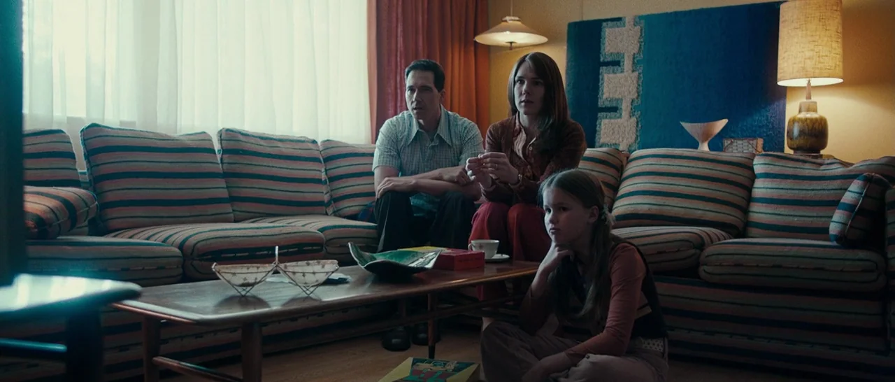 Pawn Sacrifice (2014) movie still: wide — A 1970s living room features a large striped sectional sofa and wooden coffee table. A man and woman sit…