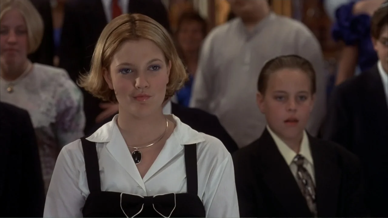 The Wedding Singer (1998) movie still: medium — A group of people stand in a brightly lit interior space with rows of seats. A woman in a black and…