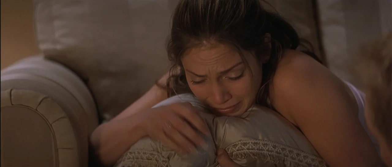 The Wedding Planner (2001) movie still: closeup — A dimly lit room features a woman lying on a plush neutral colored sofa. She rests her head on a…