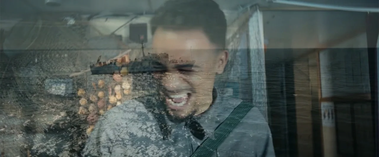 McWalter (2025) movie still: medium — A double exposure overlays a fishing boat cabin with an exterior ocean scene. A man in a collared shirt laughs…