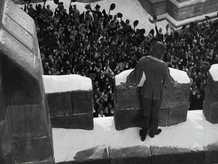 Queen Christina (1933) movie still: wide — A stone fortification is covered in snow during a cold winter day. A man stands on the ramparts looking…