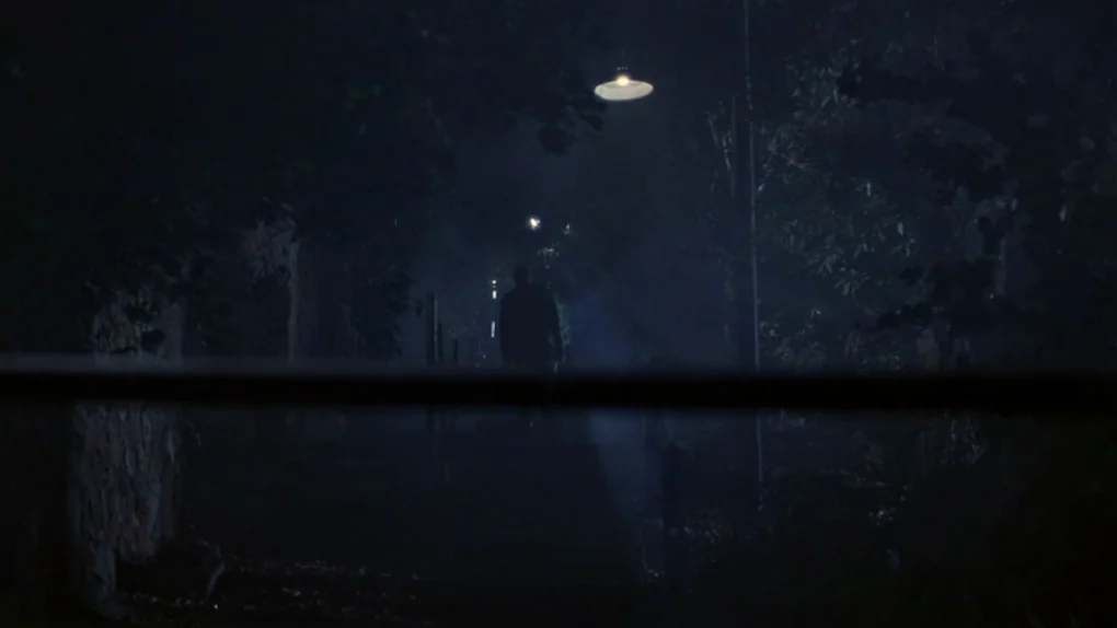 Ask The Dust (2006) movie still: wide — A dark, tree-lined suburban street at night is illuminated by a single overhead light. A lone figure in a…