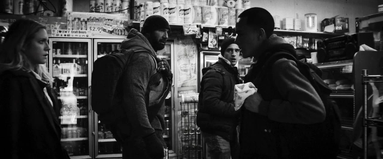 Bushwick (2017) movie still: medium — A cluttered interior of a small market filled with shelves of various goods. Four individuals are gathered in…