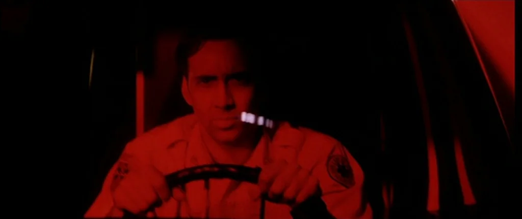 Bringing Out The Dead (1999) movie still: medium — A man in a uniform drives a vehicle at night in complete darkness. The scene is illuminated…
