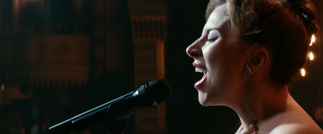 A Star Is Born (1954) movie still: closeup — A dimly lit stage features a performer standing in front of a microphone. The woman sings with her head…