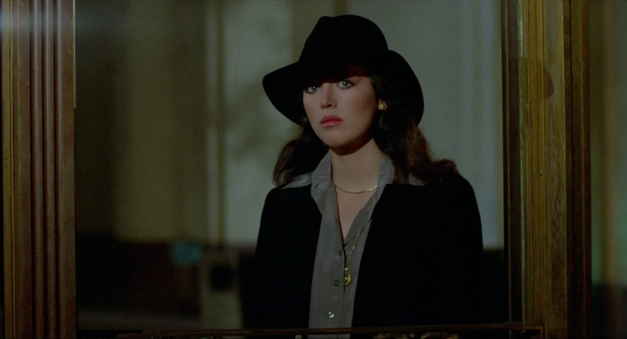 The Driver (1978) movie still: medium — A dark, dimly lit corridor features a reflective surface showing a woman's portrait. The woman wears a hat…