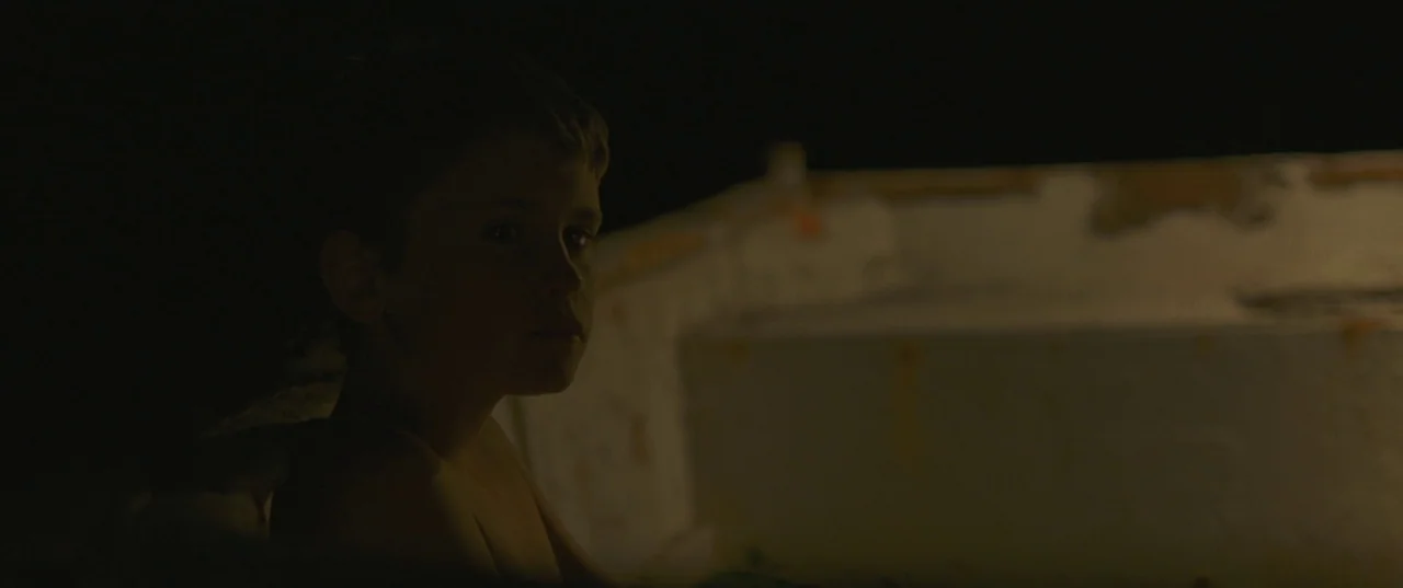 Evolution (2015) movie still: medium — The interior of a small, weathered boat at night with peeling paint. A young boy sits in the boat looking…