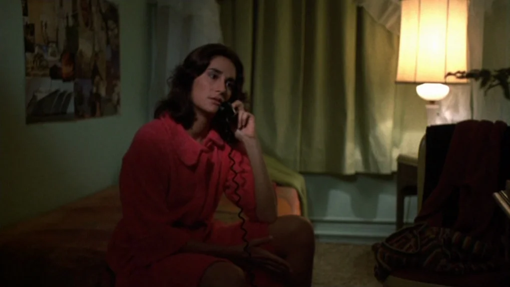 Mean Streets (1973) movie still: medium — A dimly lit room contains a bed and a vintage table lamp. A woman sits on the bed while speaking on an…