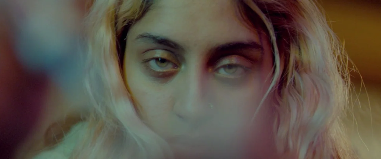 Catch Me Daddy (2014) movie still: closeup — A close portrait of a young person in a dimly lit indoor space. The subject stares ahead with a direct…