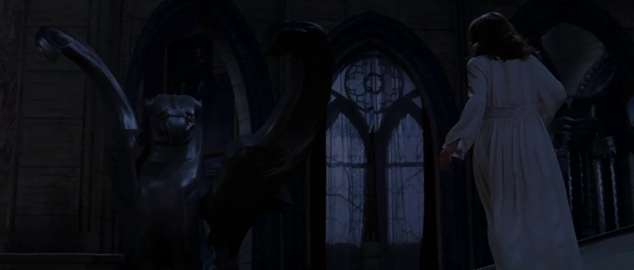 The Haunting (1999) movie still: fullbody — A dark, vaulted hallway features stone architecture and tall arched windows with patterned curtains. A…
