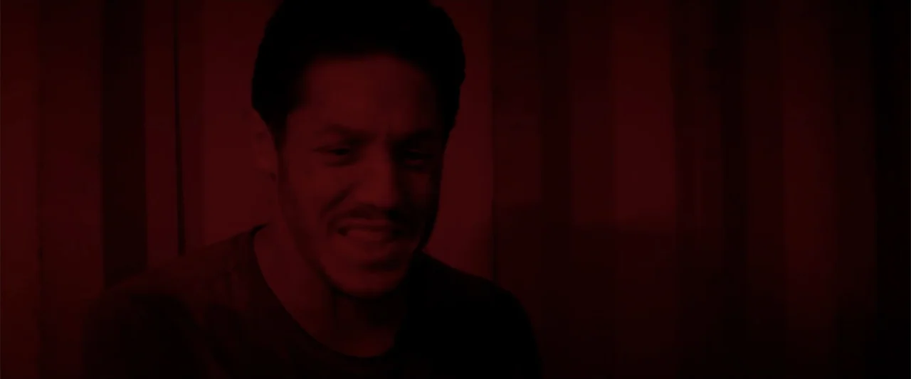 Treblinka's Last Witness (2012) movie still: medium — A dark indoor space is filled with a heavy red light saturation. A man stands in the center of…